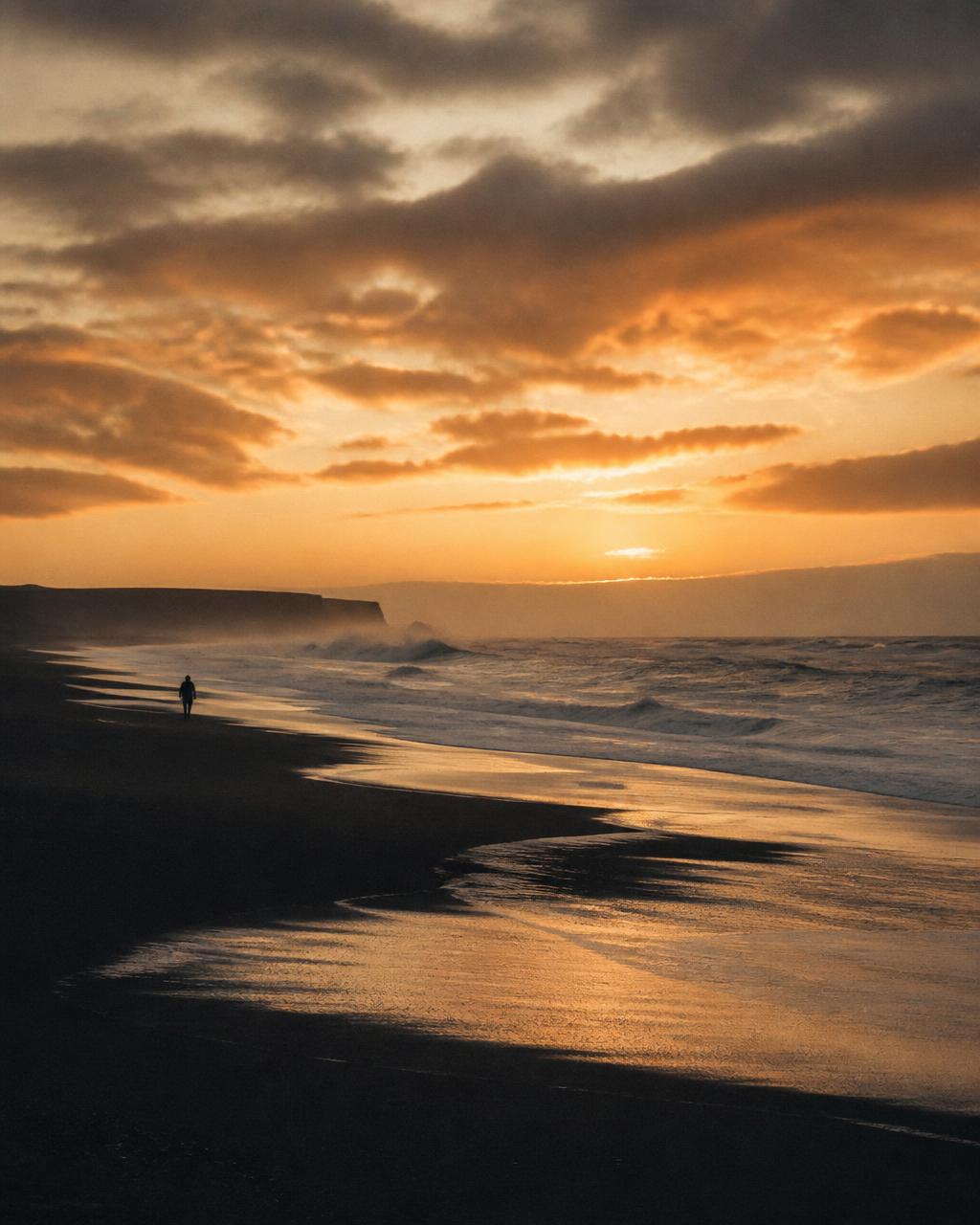 A distant figure walking a wild beach at sunrise