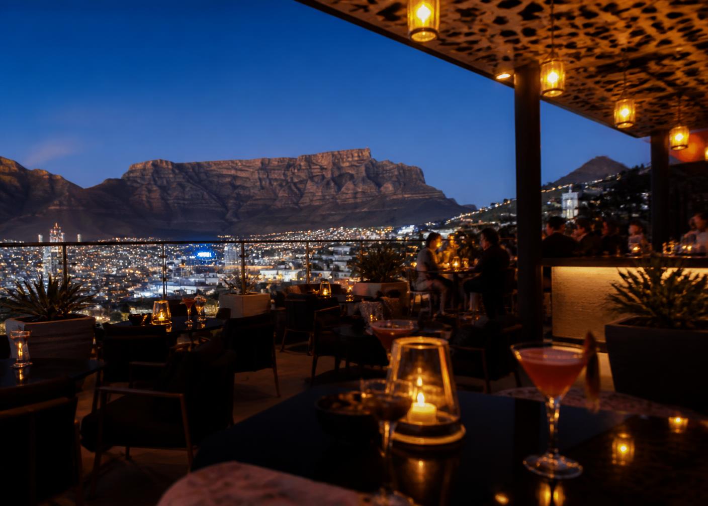 An elegant rooftop cocktail bar at blue hour with city lights