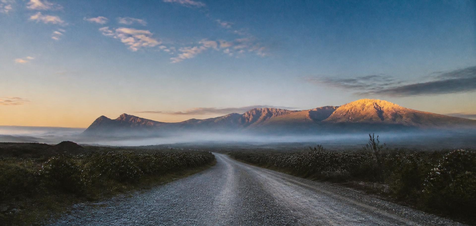 A gravel road at first light heading toward distant mountains