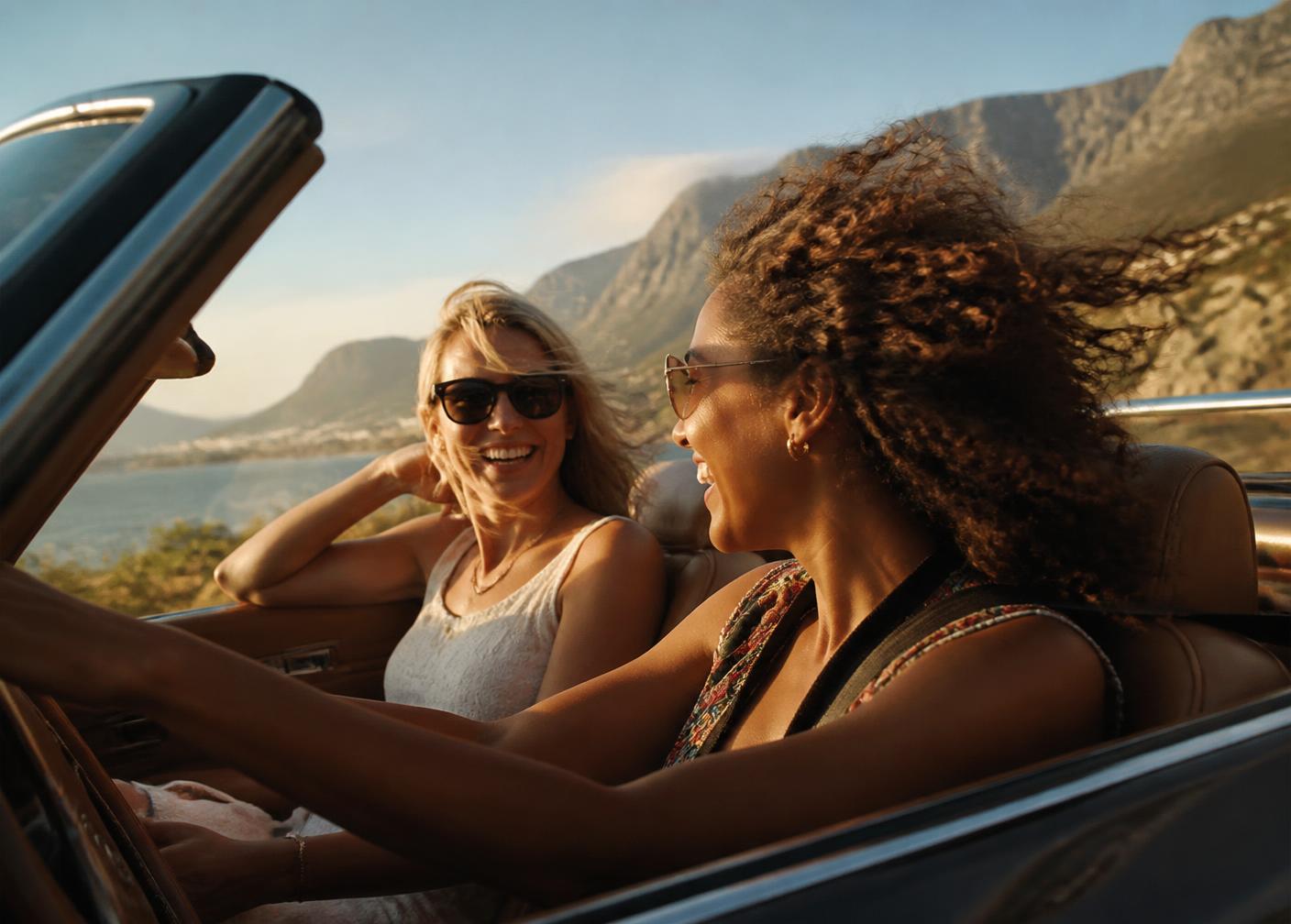 Two women in an open convertible on a coastal mountain road